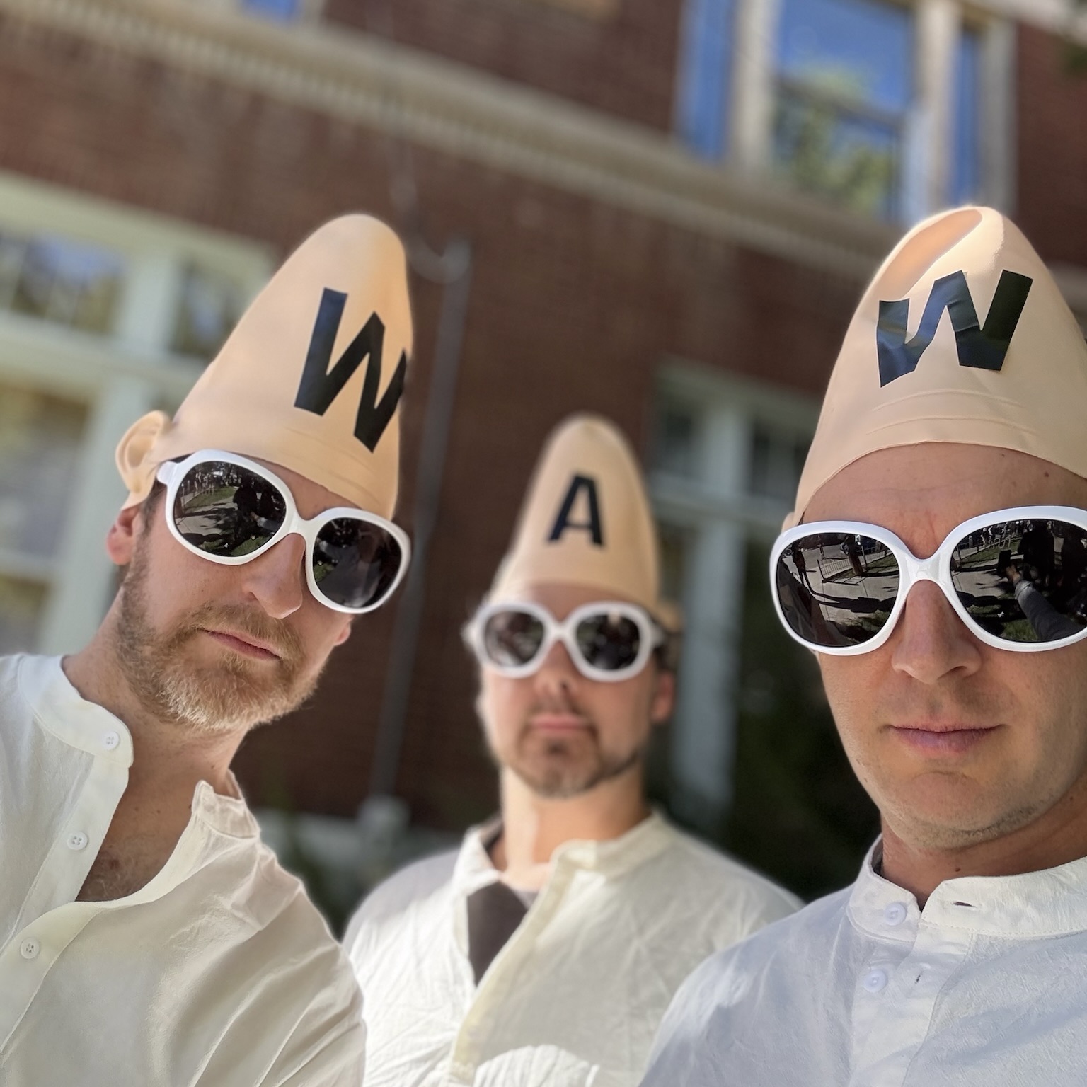 The three members of WAW wearing cone heads marked W, A and W, white sunglasses and white shirts